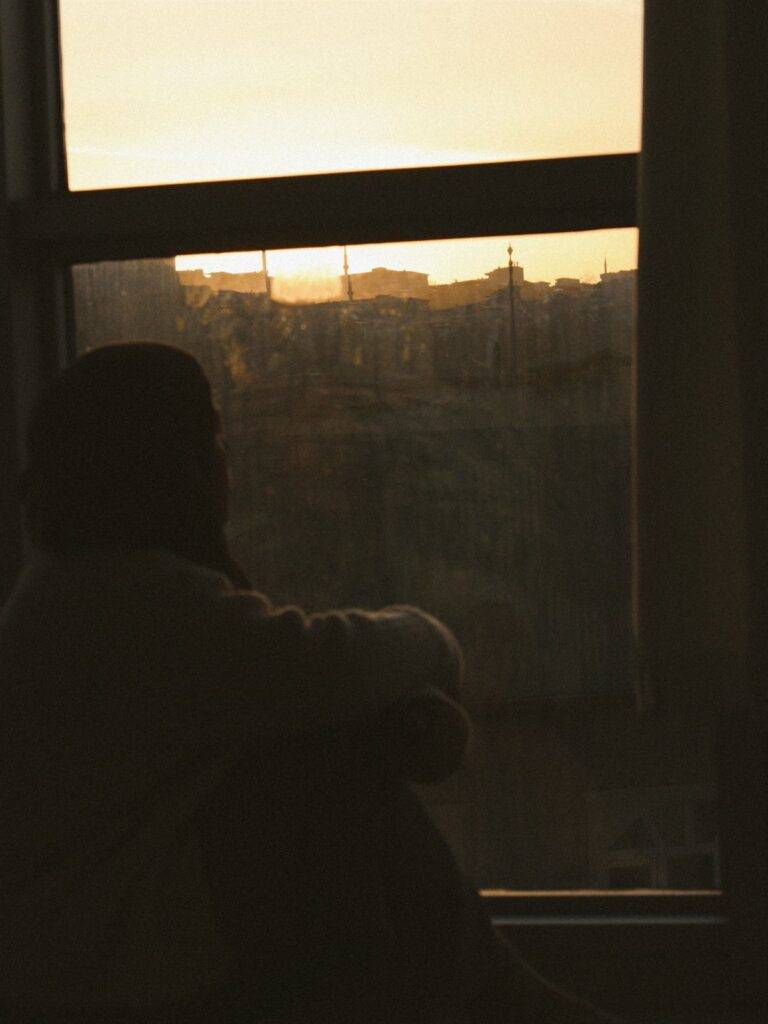 Silhouet van iemand die alleen bij het raam naar buiten kijkt bij zonsondergang