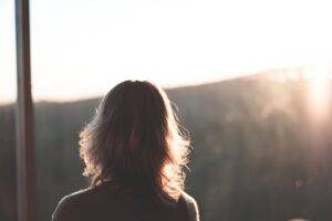 Vrouw kijkt bij zonsopgang naar buiten, met uitzicht op beboste heuvels